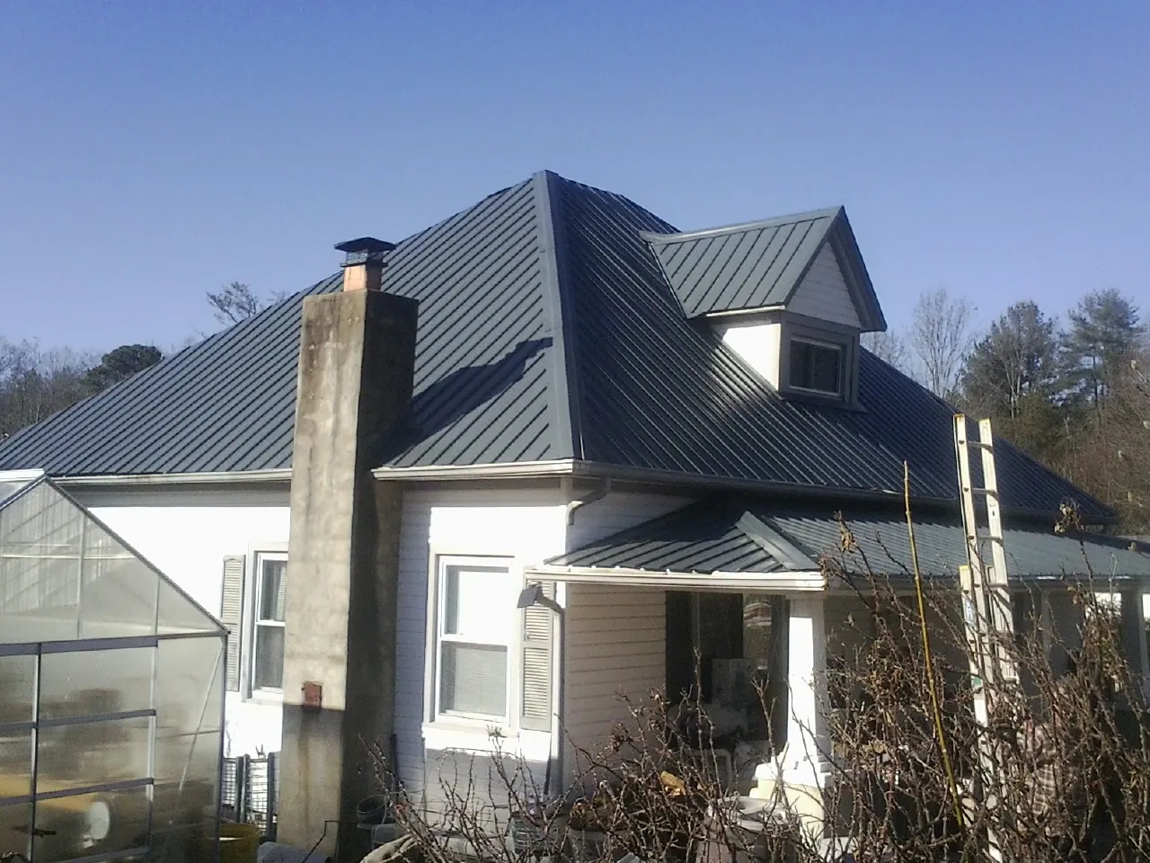 Dark blue standing seam metal roof on a white farmhouse with dormer — Slate & Tile Roof Repair by Roofing Brothers in Grimes