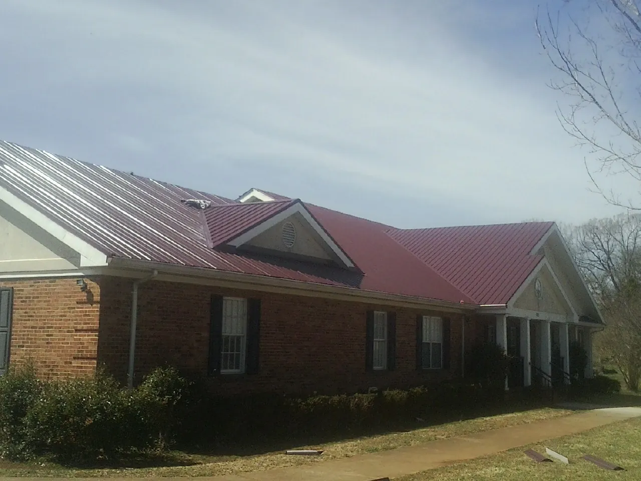 Red metal roof with gabled entries on a long brick building, from a Hail Damage Roof Repair job in Grimes