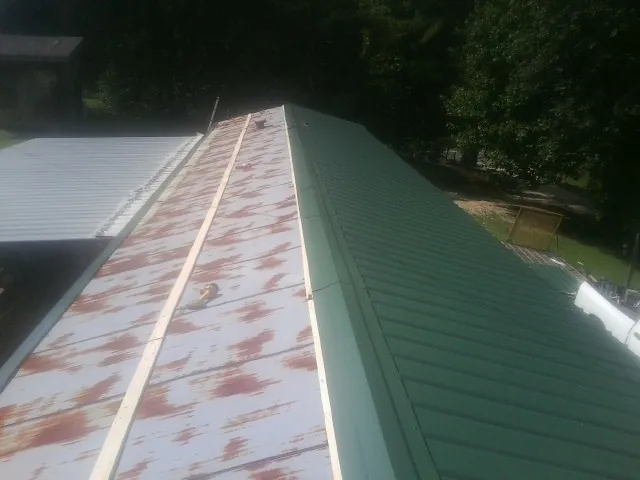 Old rusted panels beside newly installed green metal roofing — Wind Damage Roof Repair by Roofing Brothers in Grimes