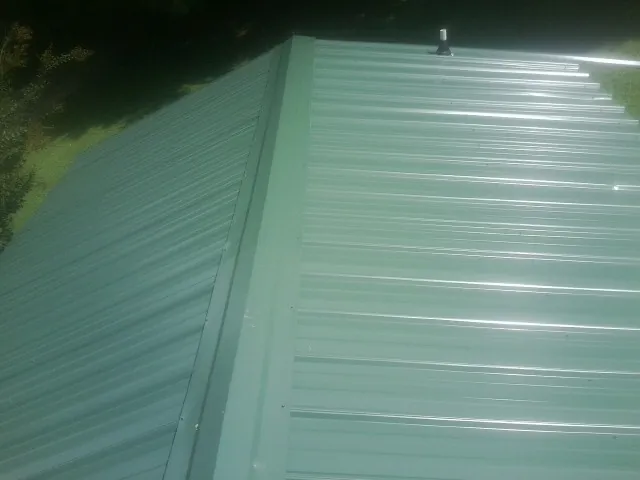 New green metal panels meeting at the ridge of a roof — Flat Roof Repair work by our crew in Grimes