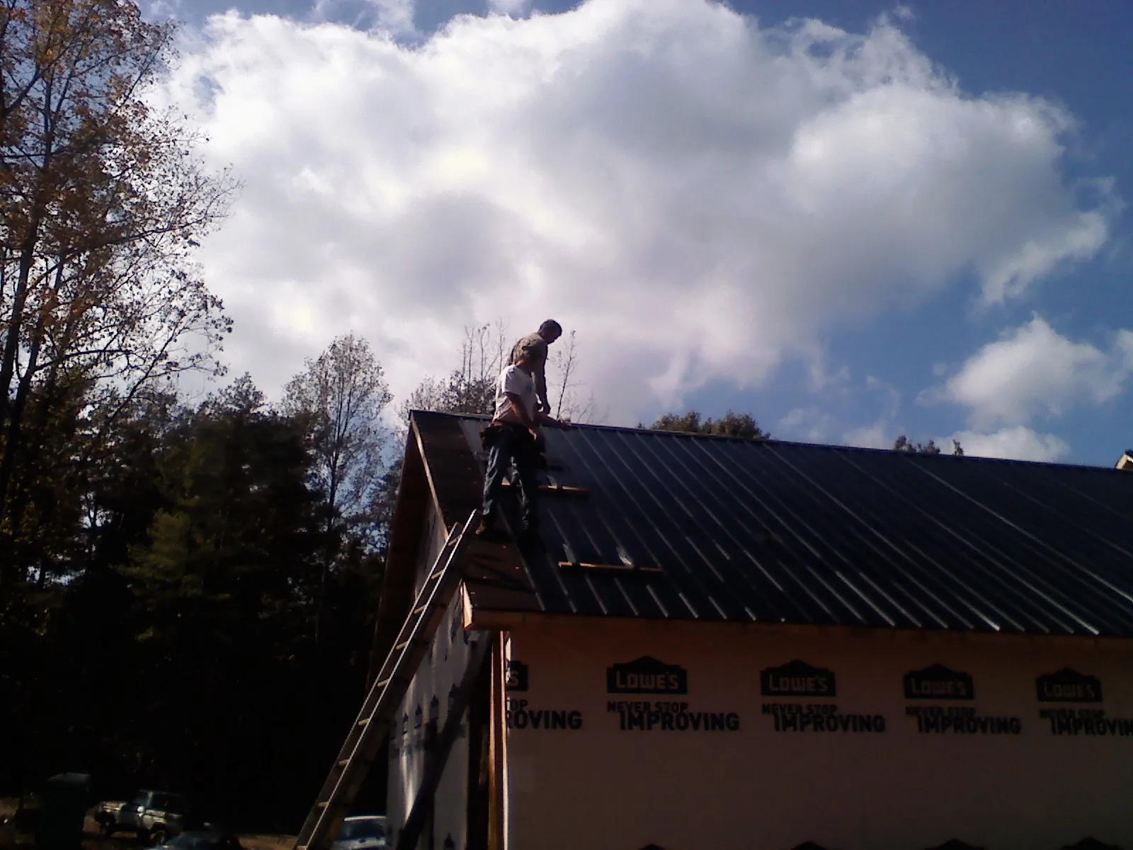 Roofer fastening dark metal panels high against a cloudy sky, from a Roof Inspection job in Grimes