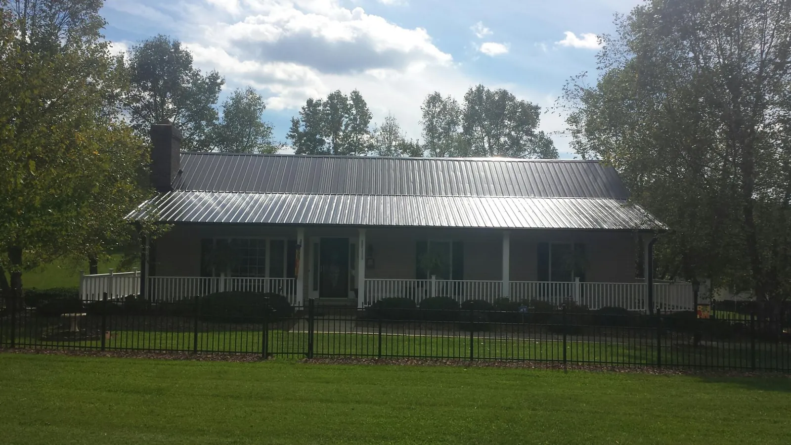 Gray metal roof on a brick ranch with a full width front porch — Gutter Guard Installation work by our crew in Grimes