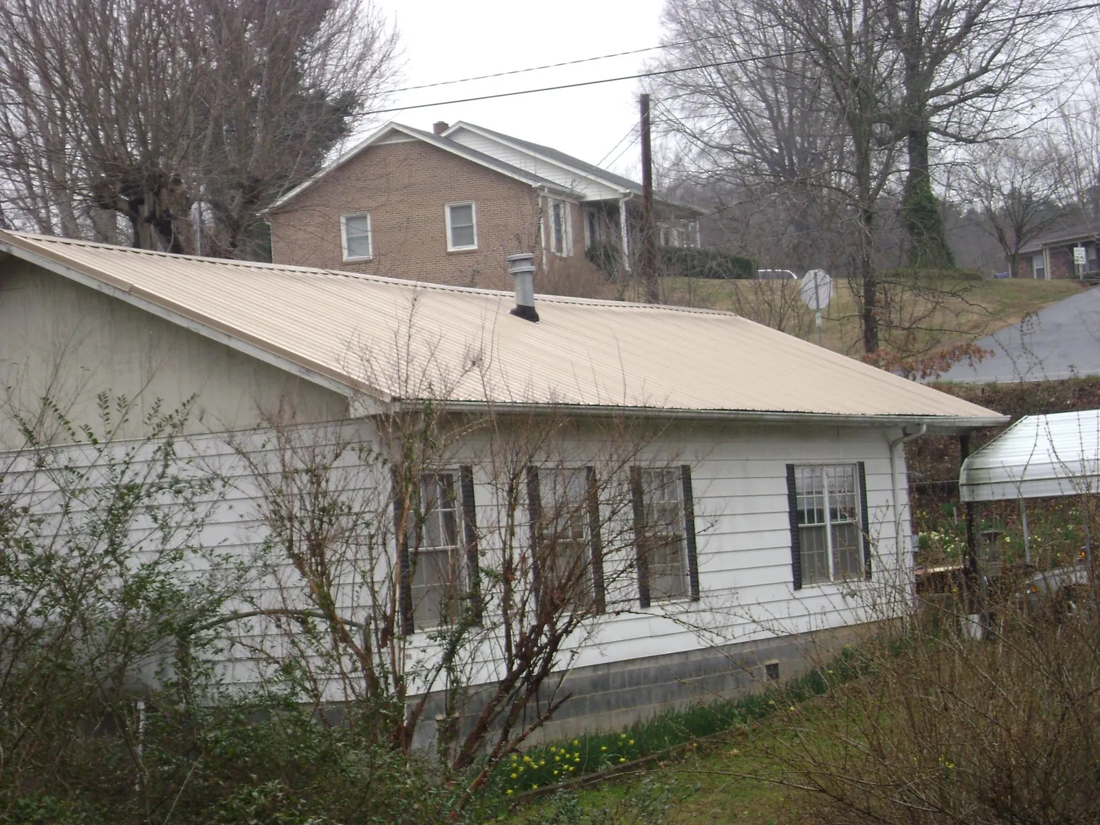 Tan metal roof on a white sided house set into a hillside — Commercial Roofing by Roofing Brothers in Grimes
